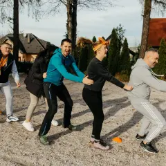 Grupa ludzi w pomarańczowych szalikach bierze udział w ćwiczeniu integracyjnym na zewnątrz.