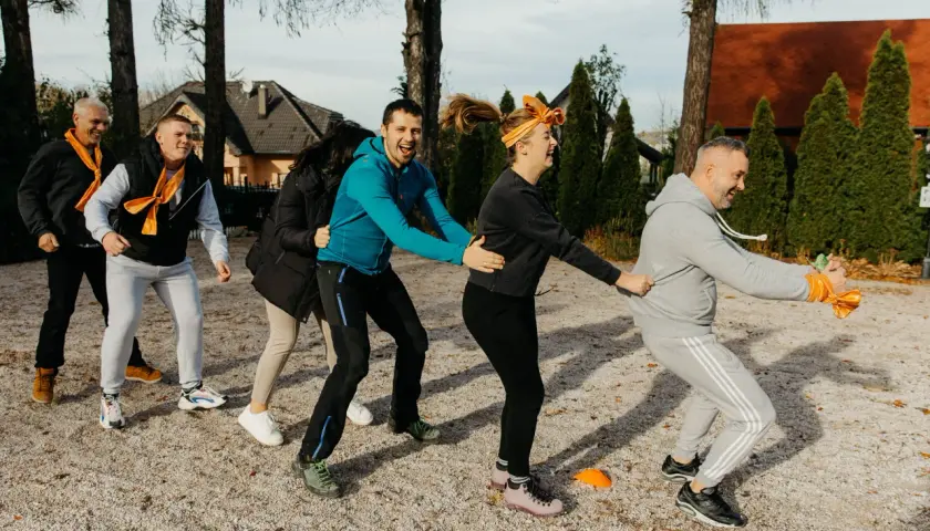 Grupa ludzi w pomarańczowych szalikach bierze udział w ćwiczeniu integracyjnym na zewnątrz.
