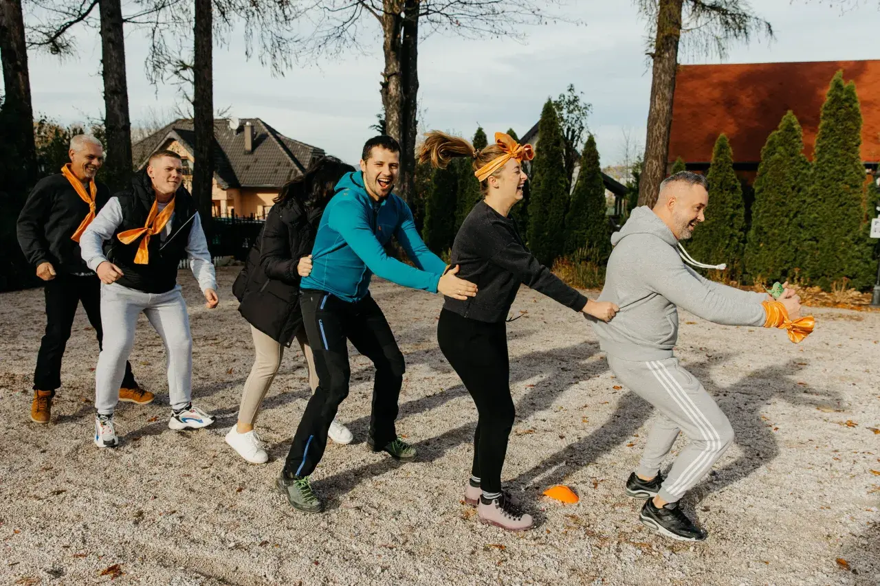 Grupa ludzi w pomarańczowych szalikach bierze udział w ćwiczeniu integracyjnym na zewnątrz.